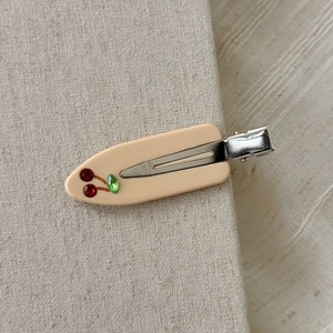 Dettaglio di un fermaglio per capelli in acetato crema con motivo a ciliegia in strass