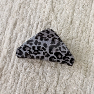 Detail view of triangular leopard print hair claw clip on soft white textured fabric