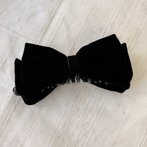 Détail d'une grande pince à cheveux avec nœud en velours noir sur un tissu texturé