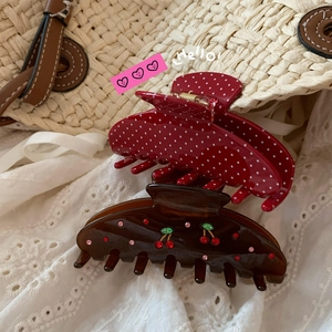 Close-up of red polka dot claw clip and amber resin cherry hair clamp set on lace