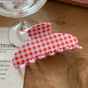 Detail of a red and white gingham checkered hair claw clip on a rustic wooden surface