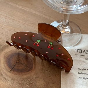 Detail of a brown translucent hair claw clip with colorful rhinestone cherry pattern