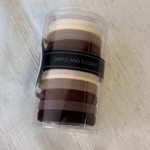 Detail of 10-piece elastic hair tie set in earth tones stored in a clear cylinder box