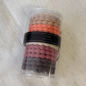 Detail of high-elasticity braided hair ties in Morandi colors inside a clear cylinder