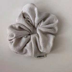 Dettaglio macro di uno scrunchie in maglia grigio chiaro scintillante con etichetta FMdrea