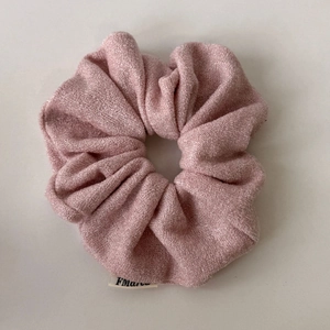 Dettaglio dell'elastico scrunchie in maglia rosa glitterata con trama metallica e etichetta