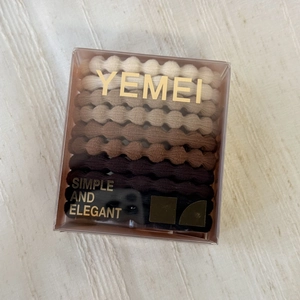 Detailed view of elastic hair ties in neutral earth tones stored in a clear square box