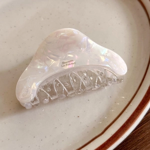 Elegant pearl white acetate hair claw clip with iridescent shell texture in a ceramic dish