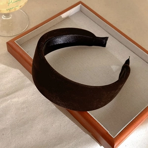 Detail of a thick dark brown velvet headband displayed on a vintage wooden tray