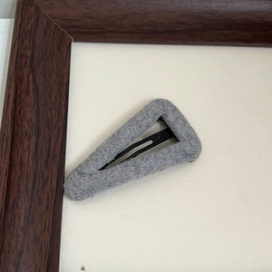 Detailed view of gray knit fabric covered triangular hair clip with sturdy metal base