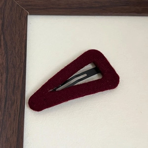 Detail of burgundy velvet-covered triangle snap clip on a white textured background