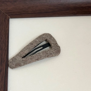 Close-up of triangle wool hair clip with grey-brown felt texture and matte metal base