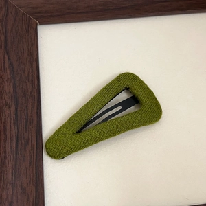 Close-up of a green knit wool triangle hair clip with textured fabric on a beige surface