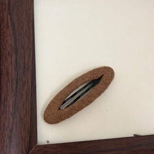 Dettaglio del fermaglio per capelli BB ovale in tessuto a maglia marrone e metallo nero