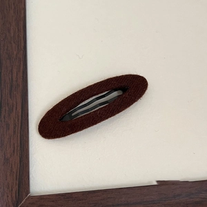 Primo piano di un fermaglio per capelli BB ovale in feltro marron caffè su fondo in legno
