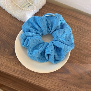 Détail d'un chouchou en tricot bleu ciel avec motif ajouré sur un plateau en céramique