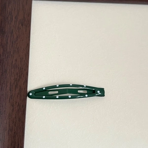 Detailed close-up of dark green metal BB hair clip with white polka dots pattern