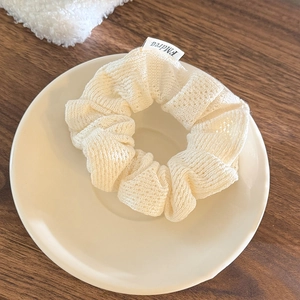 Détail montrant la texture en maille ajourée blanc crème et l'étiquette tissée du chouchou