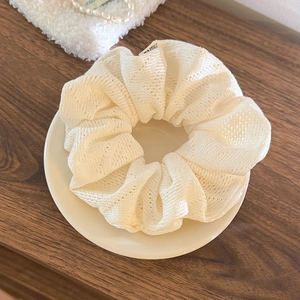Détail d'un chouchou tricoté blanc crème à texture ajourée posé sur une assiette