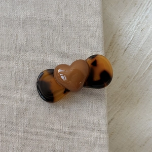 Detail of a brown heart hair clip with tortoiseshell accents on a grey linen background