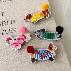 Cute embroidered dachshund dog hair clips with colorful pom poms on beige fabric background