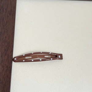 Close-up of brown teardrop-shaped metal hair clip with white polka dots on beige background