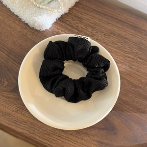 Vue détaillée d'un chouchou en tricot noir avec étiquette sur une assiette en céramique