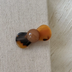 Detailed view of amber tortoise shell hair clip with mini round ball on beige fabric
