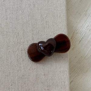 Detail of a dark brown heart-shaped acetate hair clip on rustic cream linen fabric