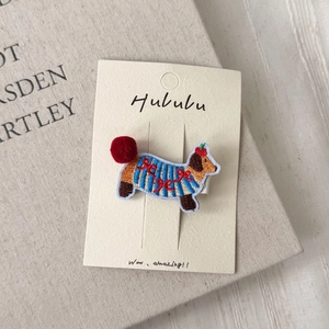 Macro shot of embroidered dachshund hair clip with 3D red pompom on original display card