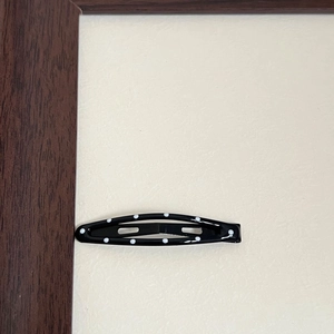 Close-up of a vintage black metal BB hair clip with white polka dots on textured background