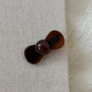 Detailed view of a brown amber texture bow hair clip on a minimalist linen background
