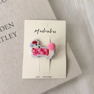 Close-up of cute embroidered dachshund hair clip with pink pom-pom on book