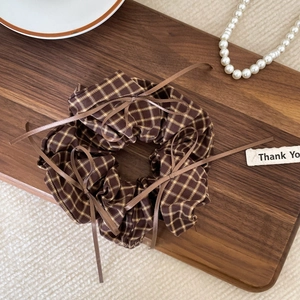 Close-up of brown plaid scrunchie with ribbons on a wooden tray with pearl decor