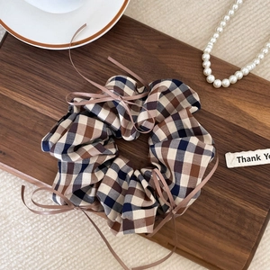 Close-up of a plaid hair scrunchie with a delicate brown ribbon bow on a wooden tray