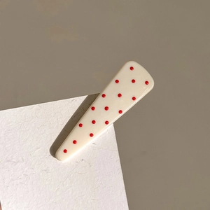 Minimalist cream hair clip with red polka dots on textured card with soft shadows