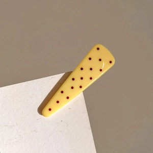 Detail shot of yellow triangular hair clip with red polka dots on white textured paper