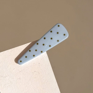 Detail of light blue triangular hair clip with golden polka dots on textured surface
