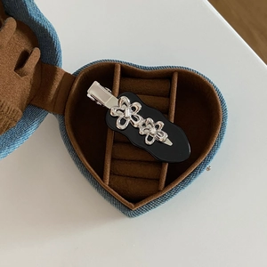 Detail of silver metal flower hair clip with rhinestones in a blue denim heart box