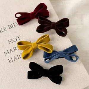 Five assorted velvet bow hair clips in retro autumn colors on a textured prop book