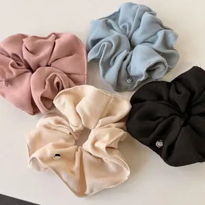 Set of four pastel large fabric scrunchies in pink, blue, beige, and black with metal charms