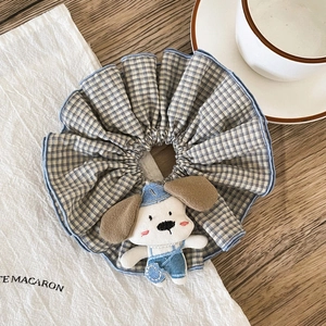 Close-up of a blue plaid scrunchie featuring a cute plush dog wearing denim overalls