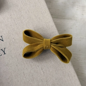 Close-up of mustard yellow velvet bow hair clip on a textured light background