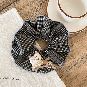 Close-up of checkered scrunchie featuring a cute 3D cat plush doll with lace collar