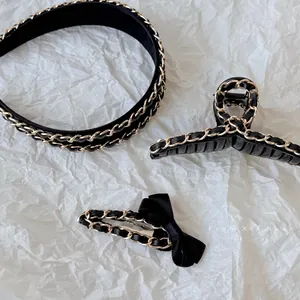 Close-up of black leather and gold chain hair accessories on white textured paper