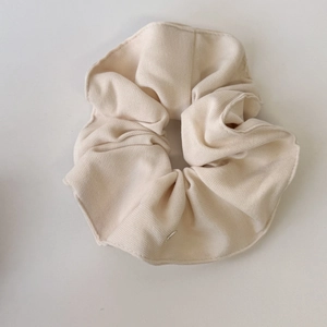 Detail of cream-colored ribbed knit scrunchie with soft pleated texture and elastic design