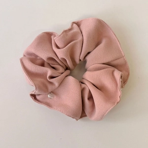 Macro detail of pink ribbed fabric scrunchie with a small silver metal logo pendant