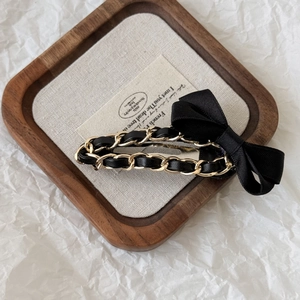 Detail of Hepburn style black leather and gold chain hair clip with a bow on linen