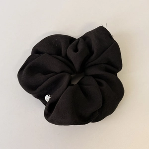 Detail of black fabric scrunchie texture with a small silver metallic brand charm
