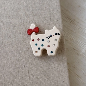 Detailed macro view of a white acetate cat hair clip with colorful rhinestones and red bow